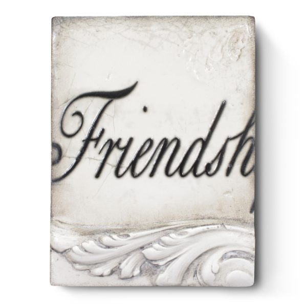 A white sculptural block decorated with 3D filigree along the bottom and the word "Friendship", with the last two letters missing, written in cursive, through the middle of the block, on it.